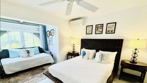 Een hotelkamer met een groot bed, een kleiner bed, twee nachtkastjes met lampen, een plafondventilator en een raam met gordijnen.