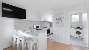 Una cucina moderna con mobili bianchi, una TV a schermo piatto, un forno a microonde, un lavello e una lavatrice.