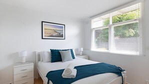 Una camera da letto con un letto, comodini, una finestra con persiane e un quadro appeso al muro.