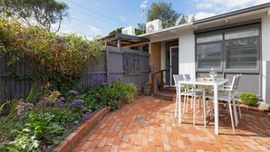 Un patio con pavimento in mattoni, mobili da esterno bianchi e un giardino con diverse piante e fiori.