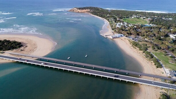 Una vista aerea di una zona costiera con un ponte, una spiaggia e edifici residenziali.