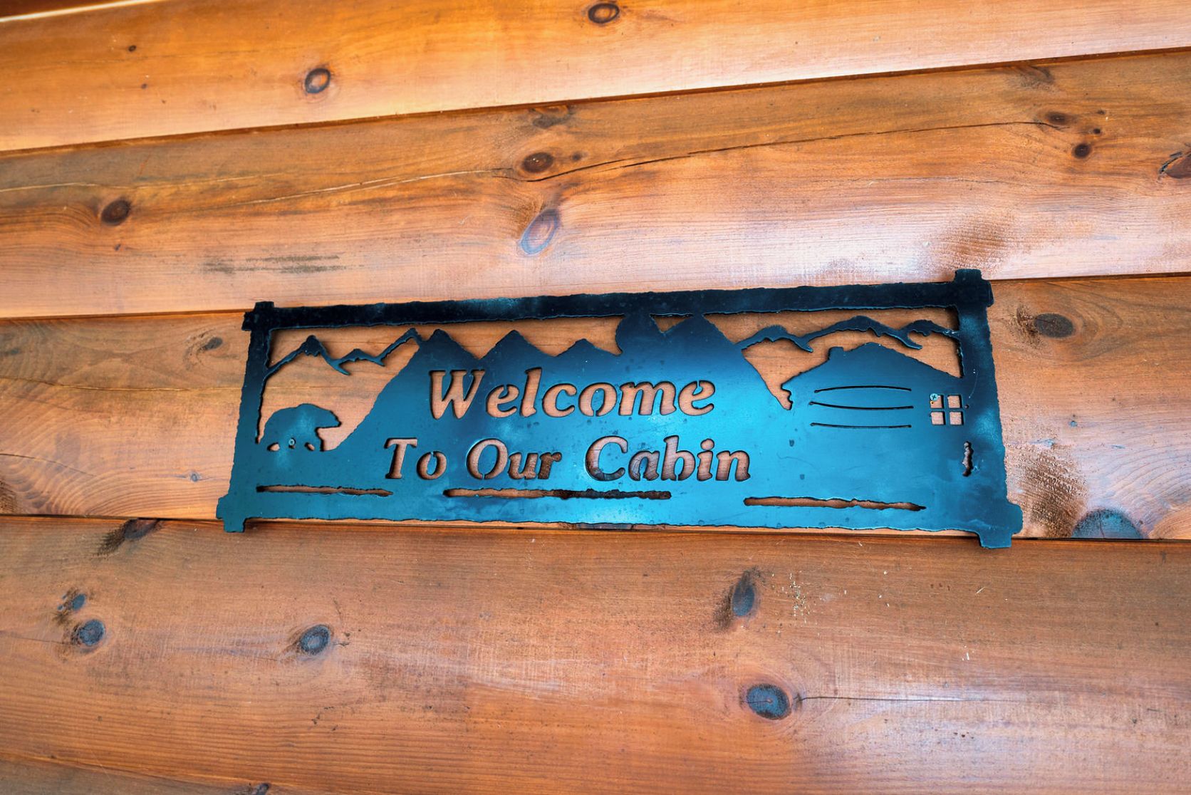 Une enseigne en bois, représentant une silhouette de montagne et portant l’inscription « Bienvenue dans notre chalet ».