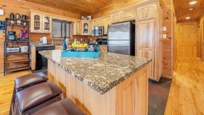 Una cocina con armarios de madera, encimeras de granito, un refrigerador de acero inoxidable e isla azul con un frutero.