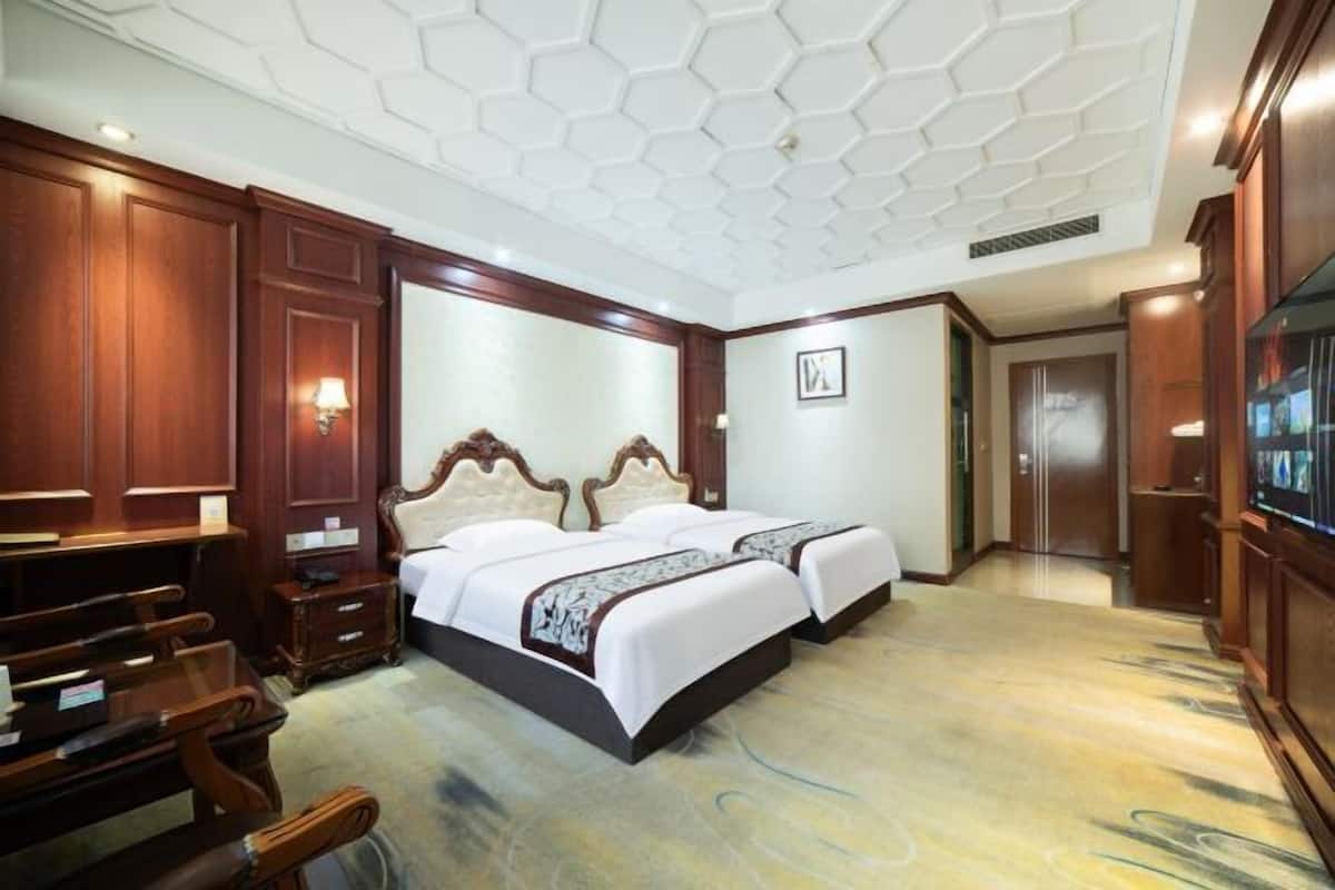 Una habitación de hotel con una cama grande, muebles de madera, un techo con diseño geométrico y un televisor en la pared derecha.