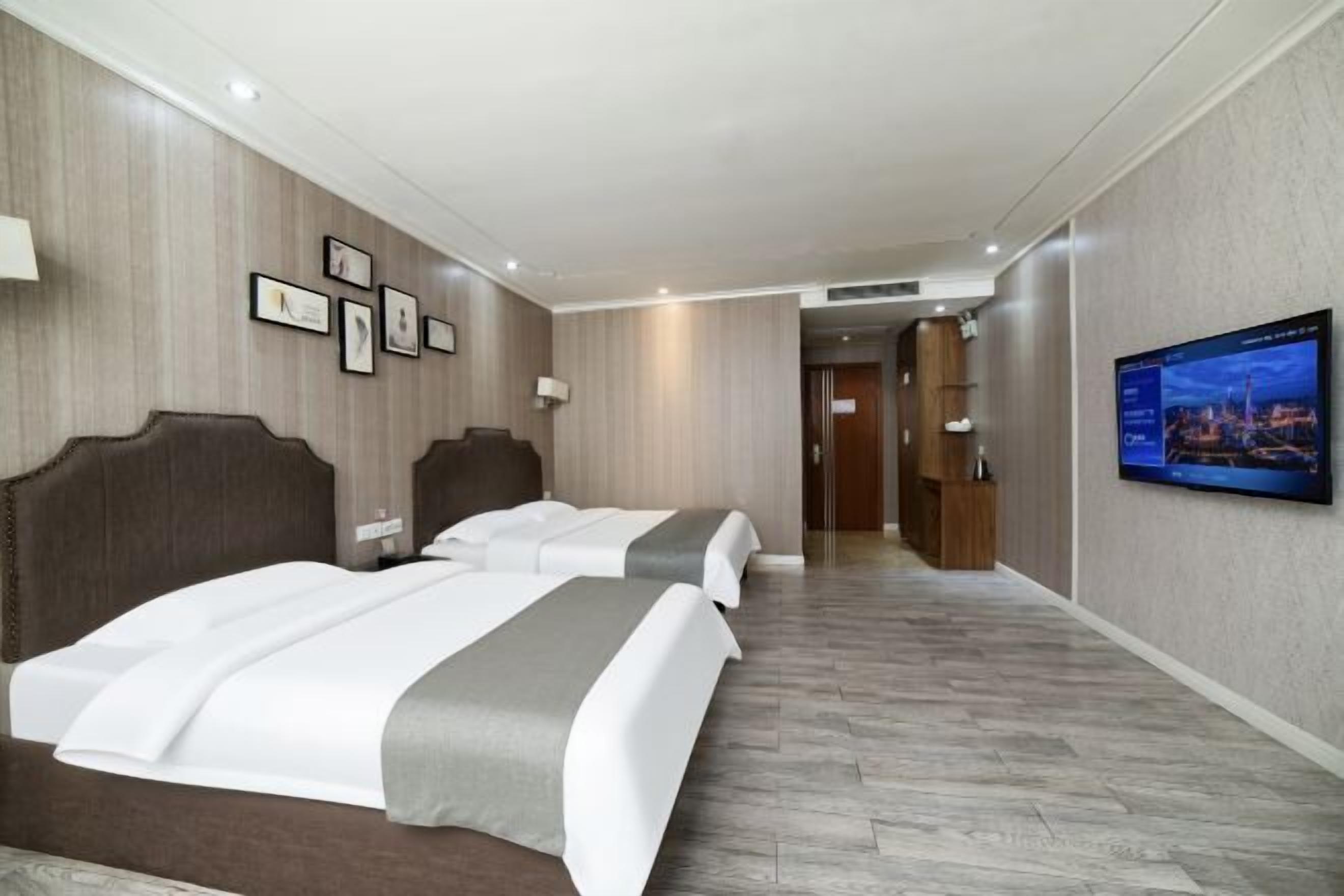 Een hotelkamer met twee bedden, een televisie aan de muur en een houten vloer.