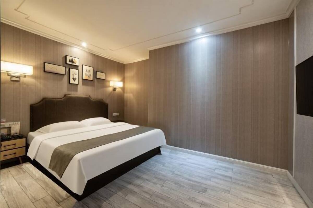 Una habitación de hotel con una cama grande, mesitas de noche, lámparas de pared y un televisor de pantalla plana.