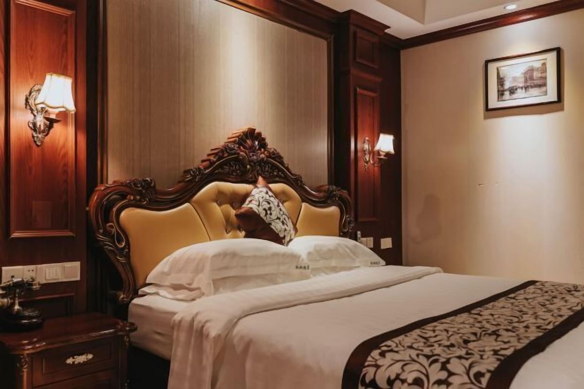 A hotel room with a large bed, wooden headboard, and wall-mounted lamps.