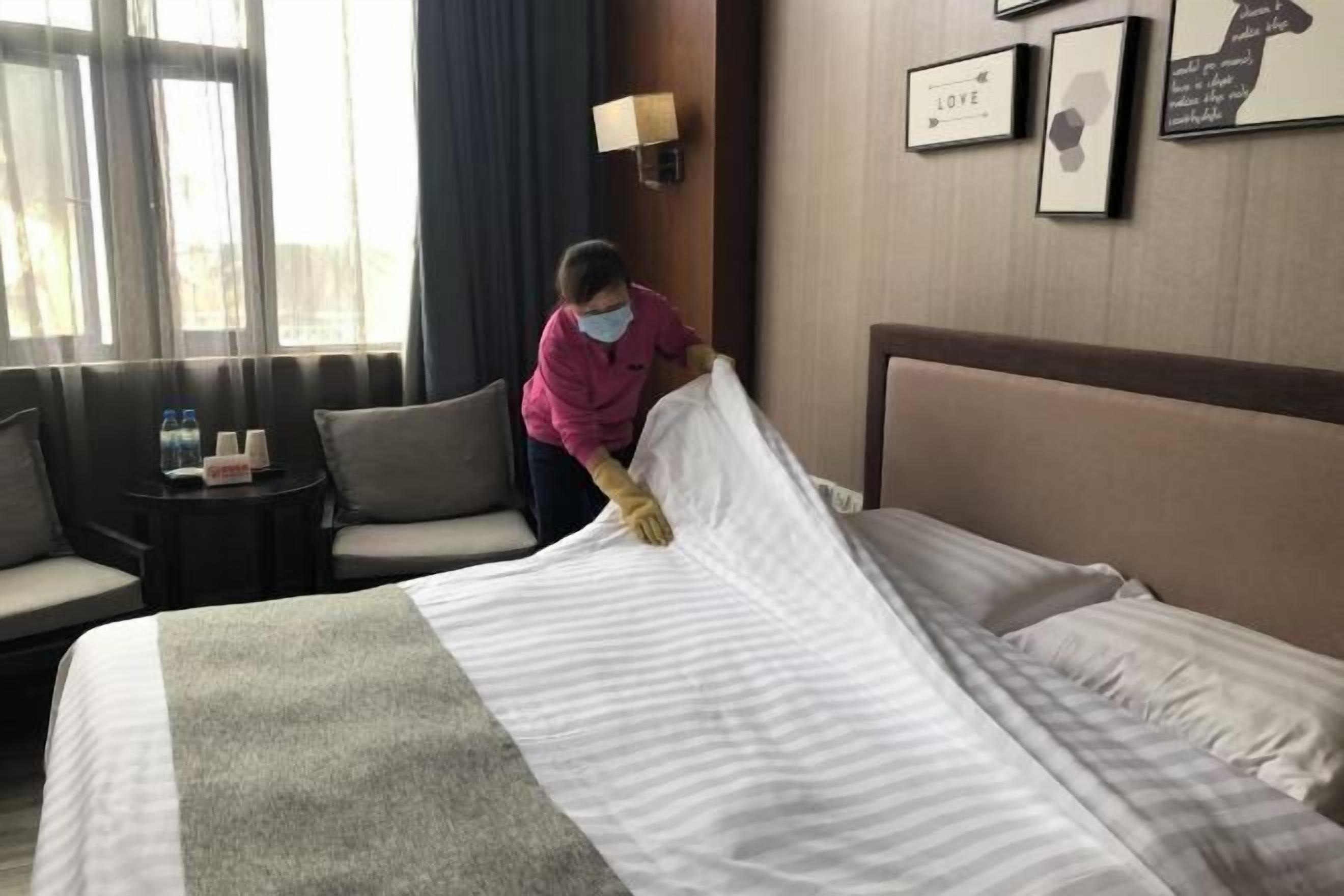 A hotel room with a neatly made bed, a sofa, a small table with water bottles, and framed artwork on the wall.