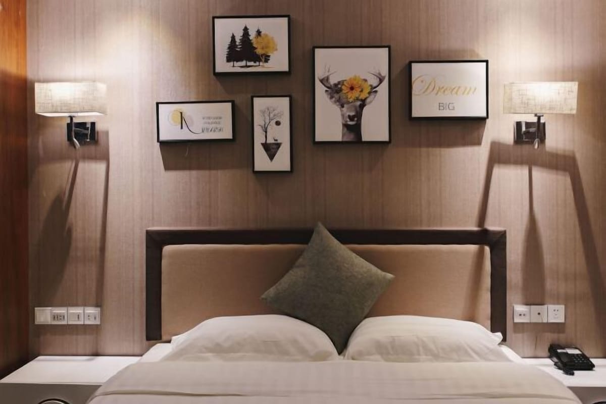 A hotel room with a bed, two bedside lamps, a nightstand, and a wall with framed pictures.
