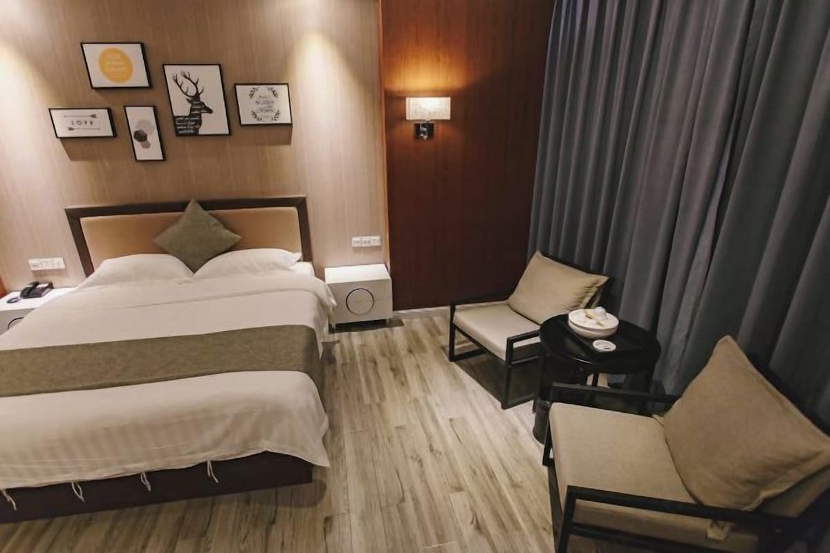 A hotel room with a large bed, a bedside table, a chair, and a wall with framed pictures.