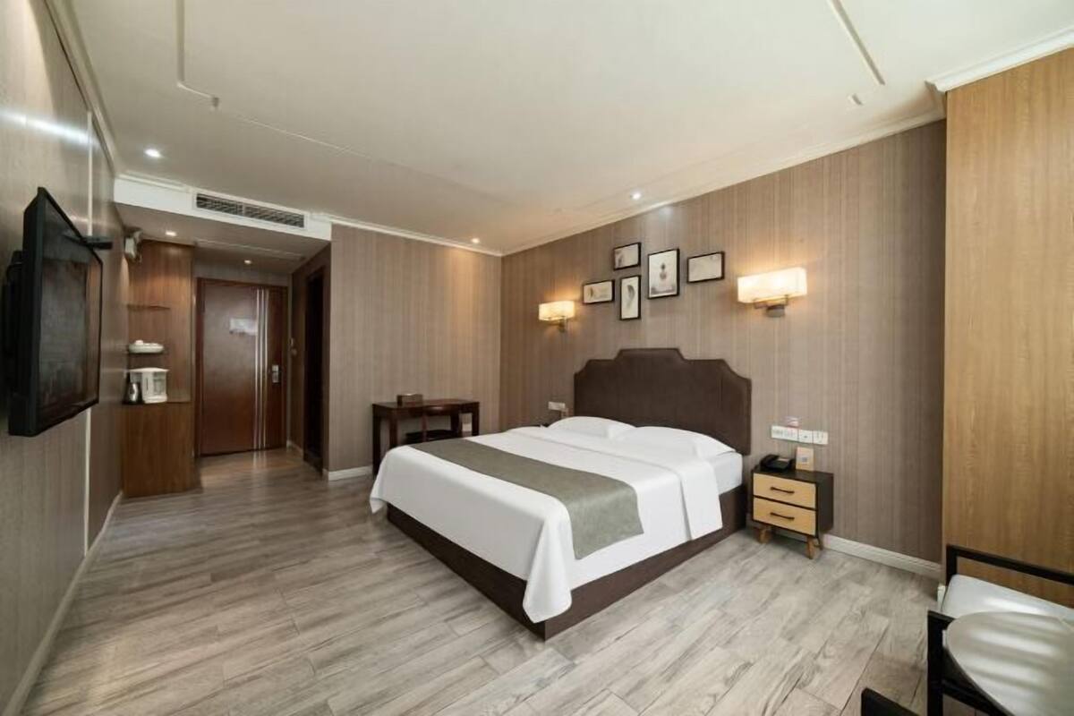 Una habitación de hotel con cama, mesita de noche, lámpara de pared y televisor de pantalla plana.