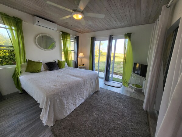 Un dormitorio con una cama grande, cortinas verdes, un ventilador de techo y un televisor sobre un mueble.