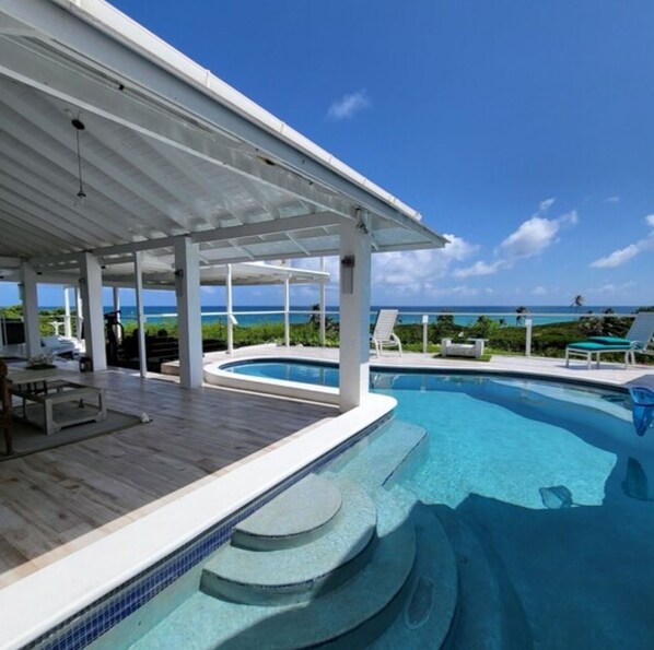 Un espace piscine avec vue sur l’océan, un patio couvert et des chaises longues.