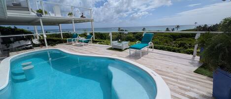A swimming pool with a deck, lounge chairs, and a view of the ocean.