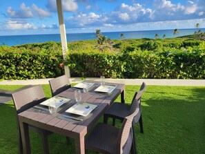 Un espace de restauration en plein air avec une table dressée pour quatre personnes, entouré d’une végétation luxuriante et offrant une vue sur l’océan.