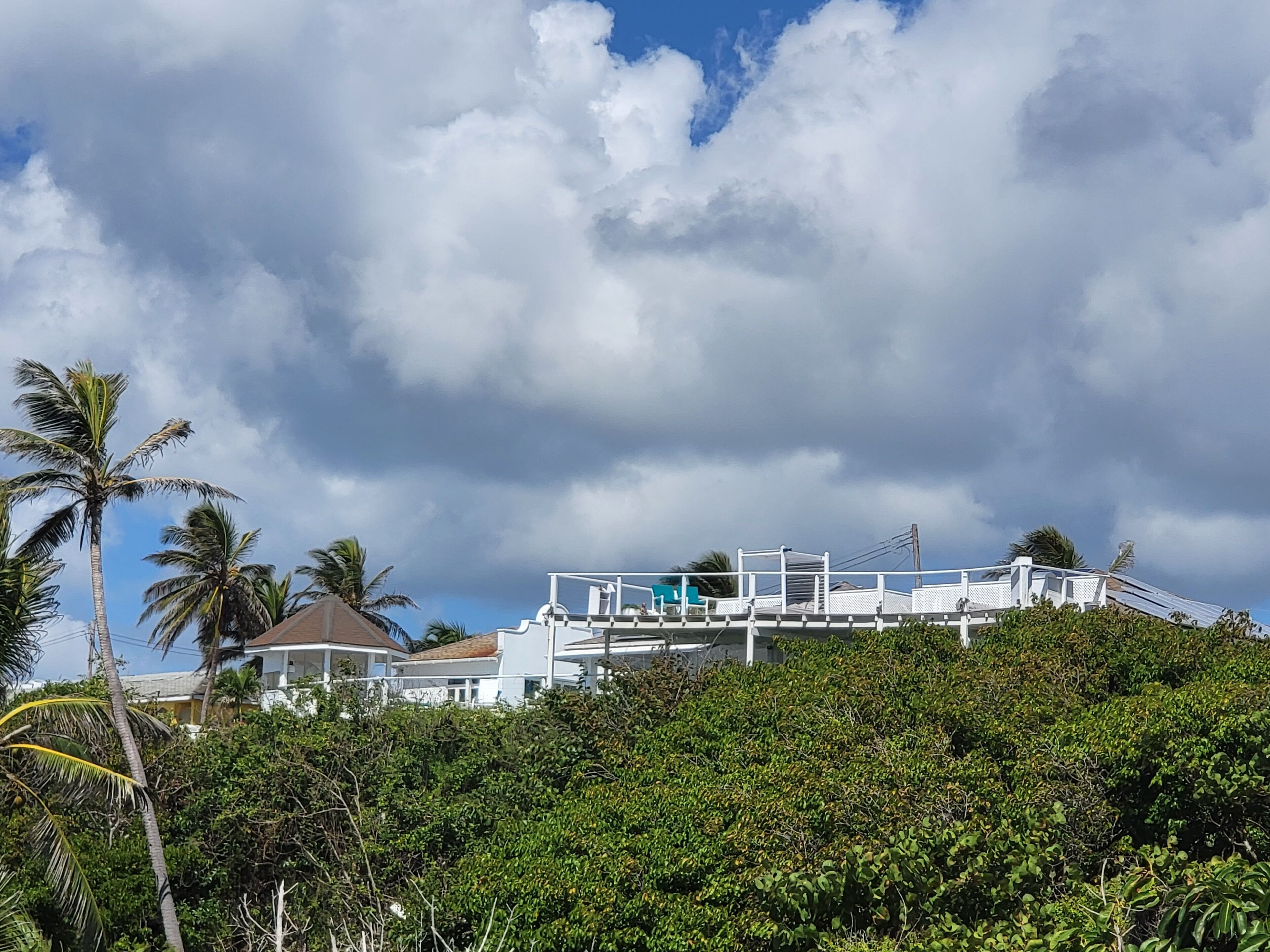 A white building with a balcony overlooking lush greenery and a cloudy sky.