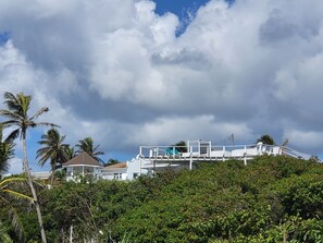 Un bâtiment blanc doté d’un balcon qui offre une vue sur une végétation luxuriante et un ciel nuageux.