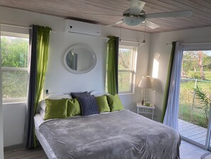 Une chambre à coucher avec un lit, un ventilateur de plafond, un miroir rond et une fenêtre avec des rideaux.