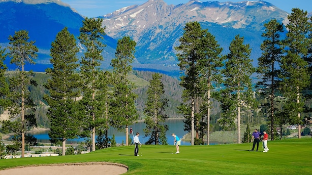 Un parcours de golf avec un lac et des montagnes en arrière-plan.