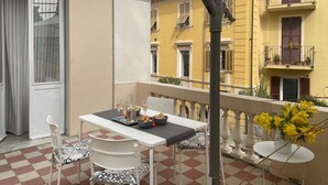 A balcony with a table set for two, a chair, and a small round table with a vase of yellow flowers.
