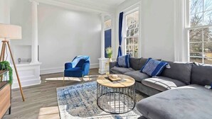 A modern living room with a grey sofa, blue armchair, and a round coffee table. - Casa Soleada in Heart of East Rock 3BR | Cozy King Bed | Near DT/Yale (New Haven)