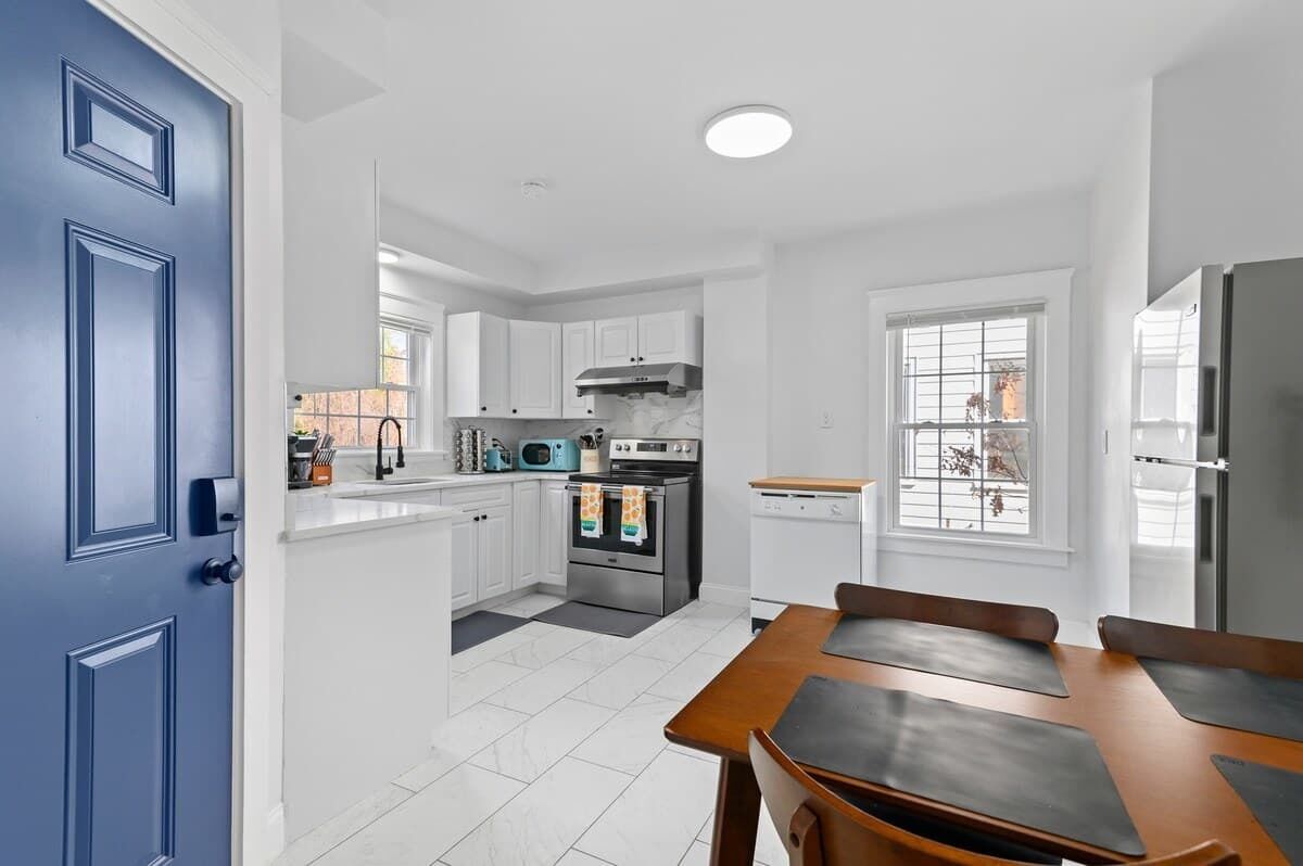 Una cocina moderna con gabinetes blancos, horno empotrado, microondas y refrigerador.