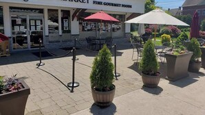 An outdoor seating area with tables and chairs in front of a building labeled "Nica's Market Fine Gourmet Foods." - Casa Soleada in Heart of East Rock 3BR | Cozy King Bed | Near DT/Yale (New Haven)
