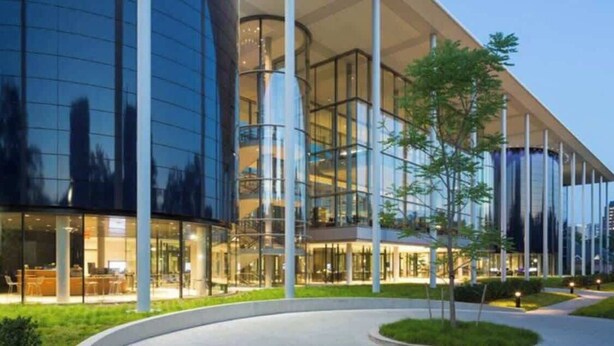 A modern building with large glass windows, a curved entrance, and a well-lit outdoor area with trees. - Casa Soleada in Heart of East Rock 3BR | Cozy King Bed | Near DT/Yale (New Haven)