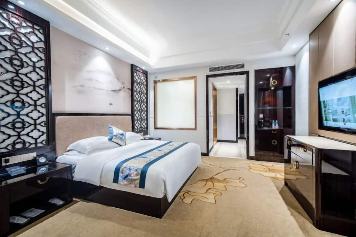 A modern hotel room with a large bed, a TV, a desk, and a wardrobe.