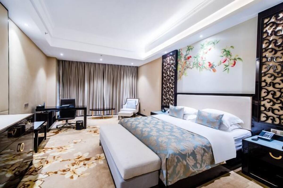 A modern hotel room with a large bed, a desk, a chair, and a TV.