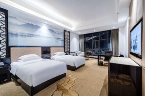 Quarto de hotel com duas camas, uma mesa, uma televisão e uma janela grande com vista.