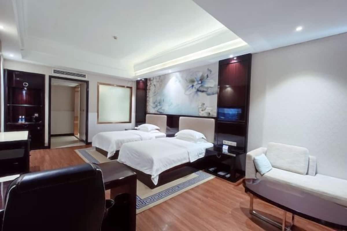 A hotel room with two beds, a sofa, a desk, and a TV.