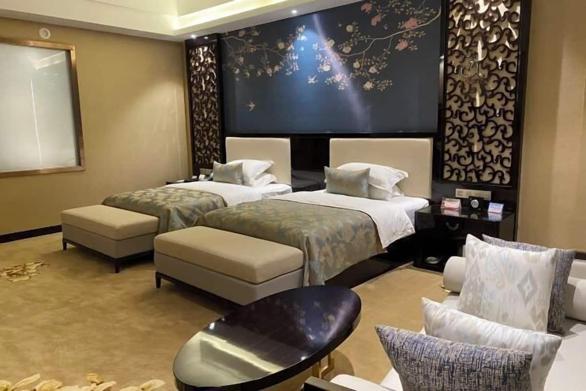 A hotel room with two beds, a sofa, a chair, and a decorative wall with floral patterns.
