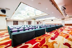 A conference room with rows of tables and chairs, a patterned carpet, and a large chandelier.