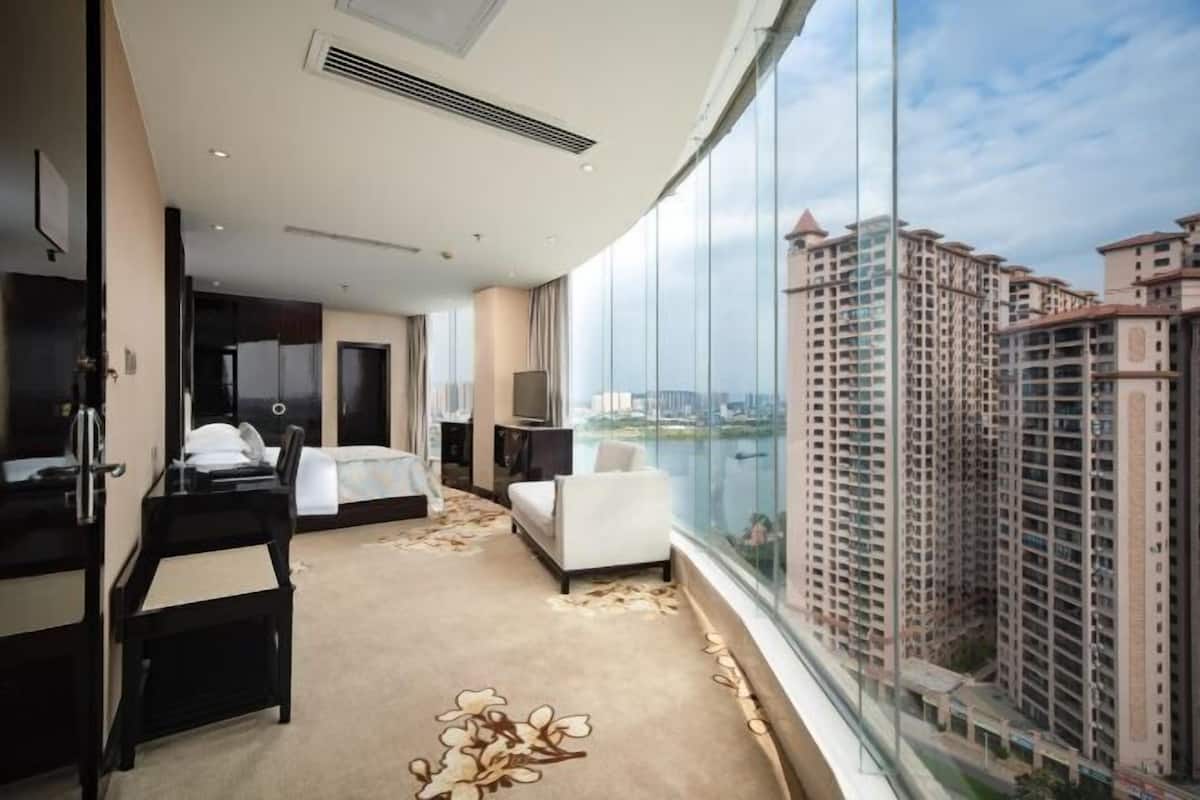 A hotel room with a bed, a desk, a chair, a TV, and a large window offering a city view.