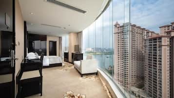 Habitación de hotel con cama, escritorio, silla, televisor y un amplio ventanal con vista a la ciudad.