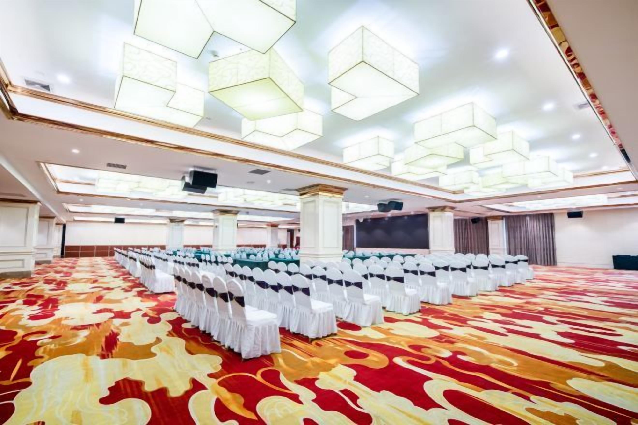 A large hall with rows of chairs and a patterned carpet, with a modern ceiling design.