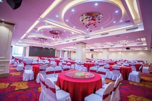 Un salón de banquetes con mesas redondas, sillas blancas y manteles rojos.