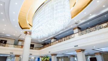 A grand hotel lobby with a large chandelier, multiple floors, and a decorative railing.