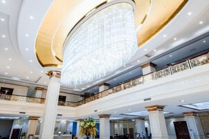 A grand hotel lobby with a large chandelier, multiple floors, and a decorative railing.