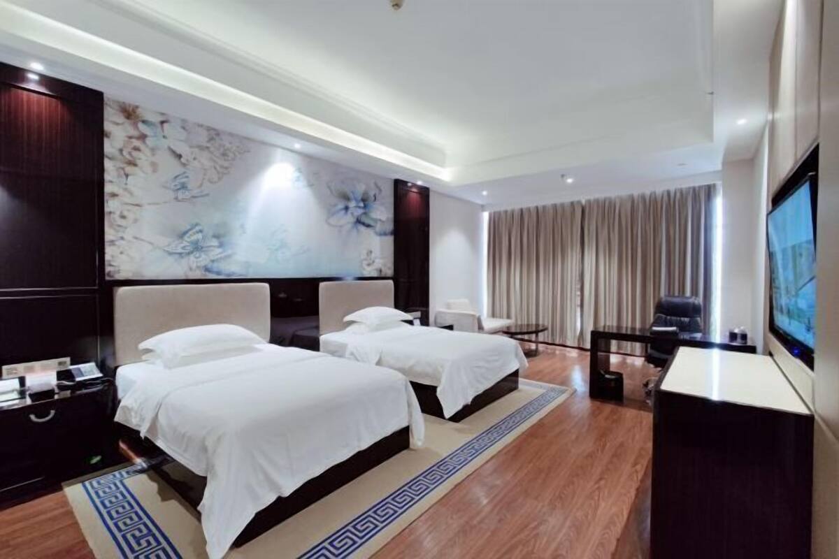 A hotel room with two beds, a TV, a desk, and a large artwork on the wall.