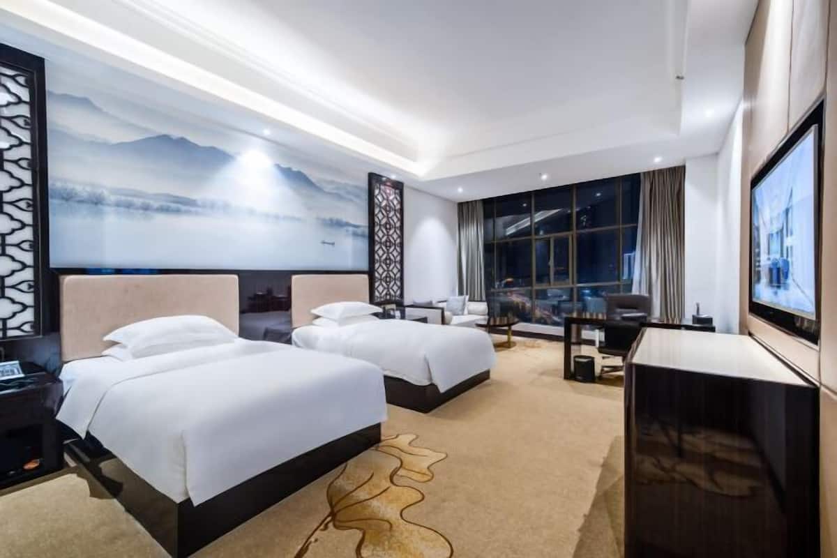 A hotel room with two beds, a desk, a TV, and a large window with a view.