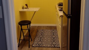 Una cucina compatta con pareti gialle, un frigorifero nero, un forno a microonde, un tavolino e un tappeto decorato.