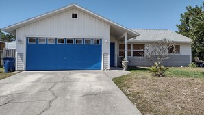 Una casa a un piano con una porta del garage blu, un piccolo portico e un giardino anteriore con un albero e una fioriera.