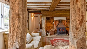 A cozy living room with a stone fireplace, wooden beams, and a view of the outdoors. - Bellflower Cottage - Ashdown Forest (Haywards Heath)