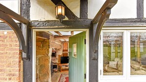 A traditional half-timbered building with a green door leading to a room with a fireplace, a television, and a red rug. - Bellflower Cottage - Ashdown Forest (Haywards Heath)