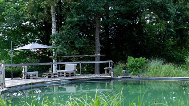 Una piscina con cubierta de madera, sillas de descanso y una pérgola.