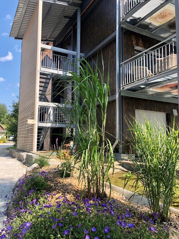 A multi-story building with a modern design, featuring balconies and a landscaped garden with purple flowers. - Lake Constance Apartment 2 – Bright 2nd Floor Apartment with Balcony and Stunning Views (Meßkirch)