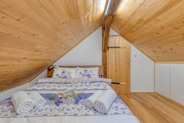 A bedroom with a sloped ceiling, wooden walls, a bed with floral bedding, and two rolled towels.