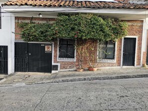 A building with a brick facade, a tiled roof, and a black gate with a 'No Parking' sign. There are potted plants in front of the building. - BLACK  ESTUDIÓ INTERIOR DE UNA CASA COLONIAL (Cali)